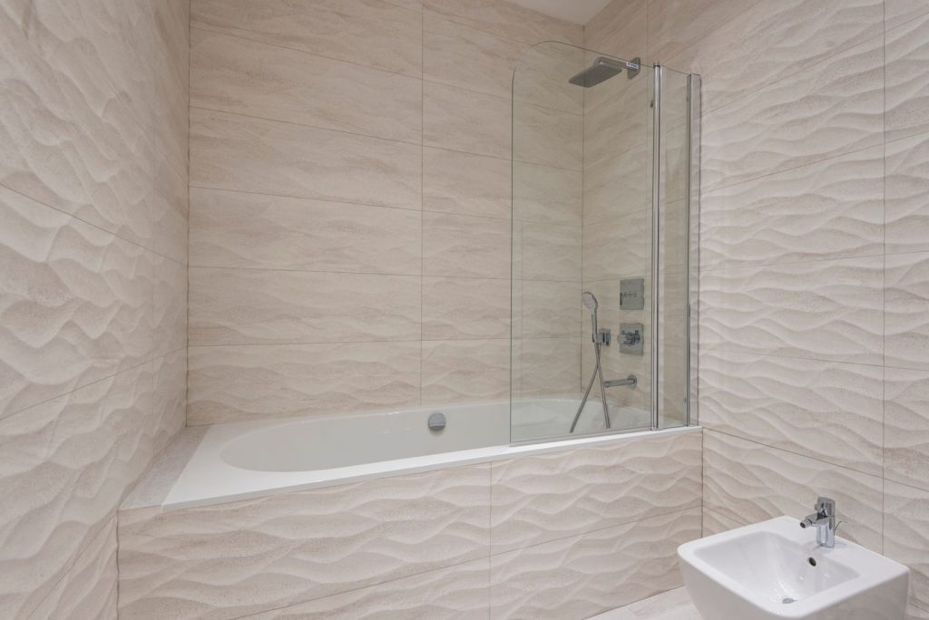 Badkamer met lichte tegels, ligbad en glazen douchewand